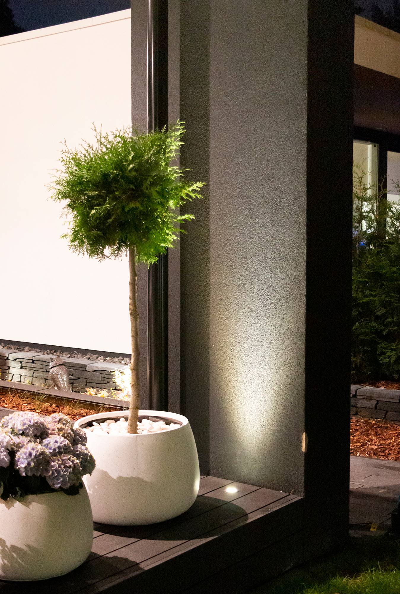 Za rostlinou a s důrazem na ni, zapuštěný květináč na terase. Reflektor osvětluje stěnu zdola nahoru nepřímým světlem. Ledstore.fi
